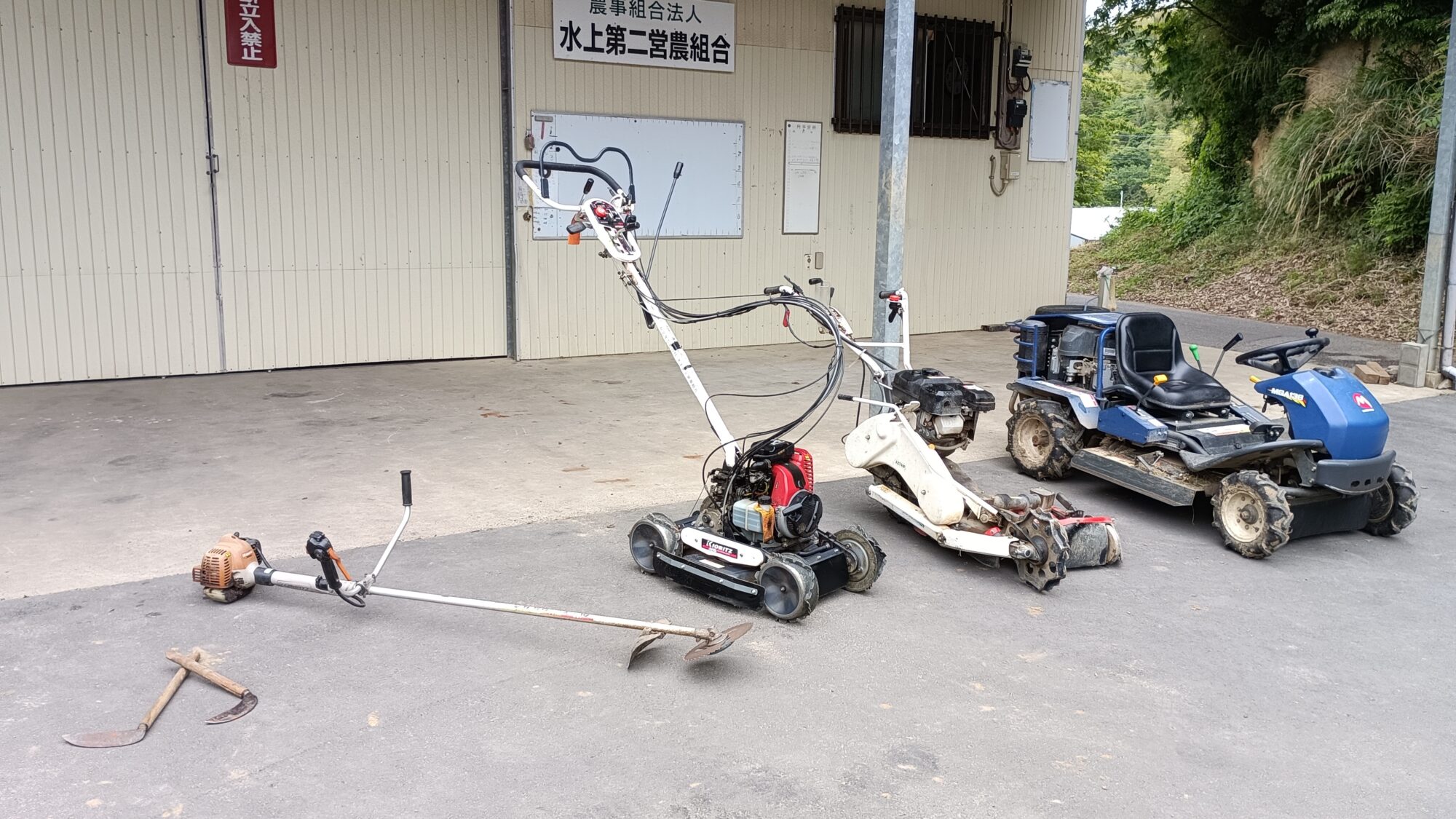 組合の草刈り道具。左より、鎌、刈払機、斜面刈機、畦刈機、乗用モア。